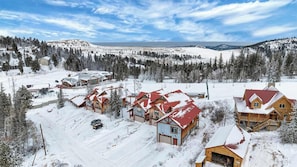 A snow-covered resort with wooden cabins, a ski lift, and a mountainous backdrop. - Homestake Slopeside Chalet at Terry Peak (Lead)