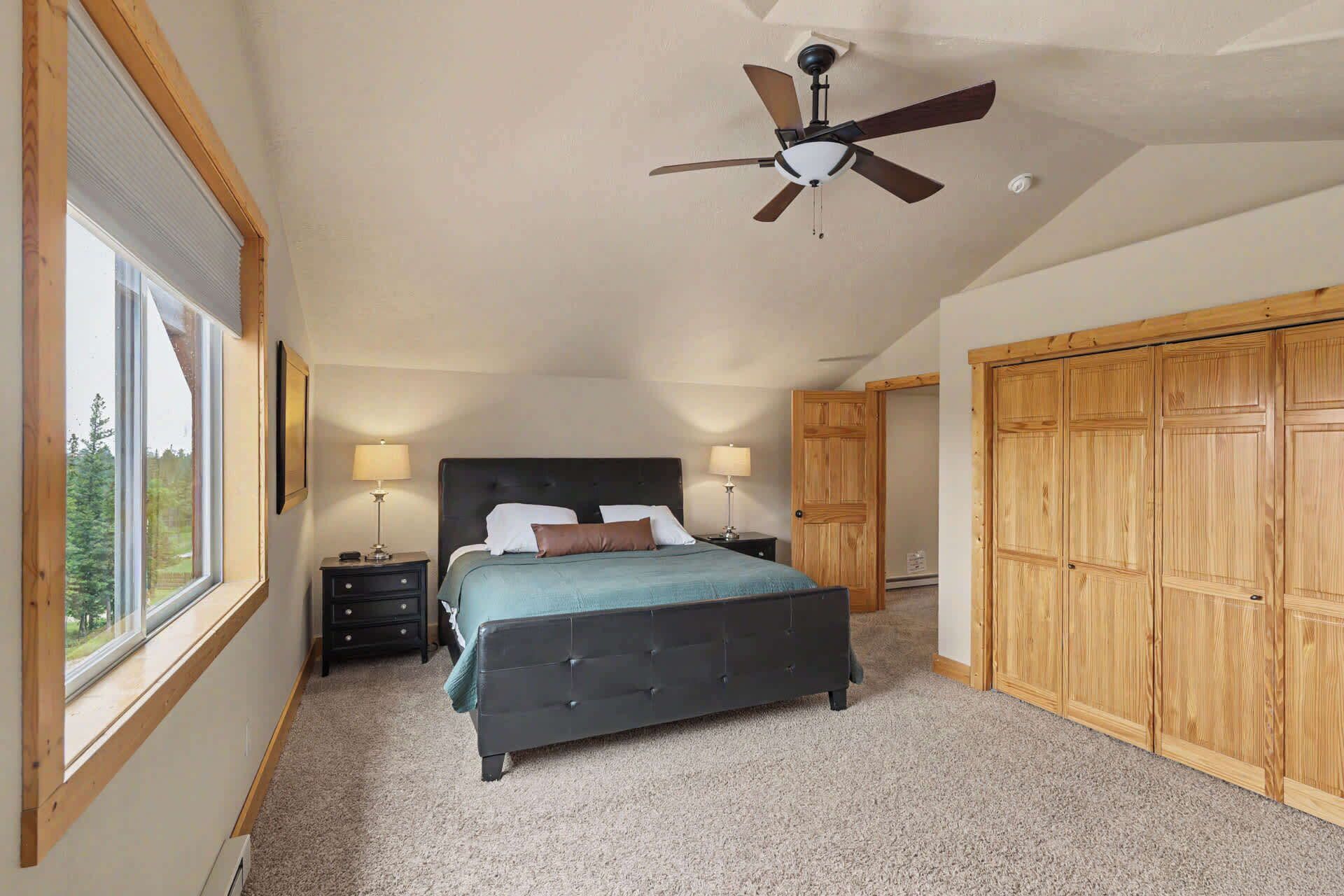 A bedroom with a bed, two bedside tables with lamps, a ceiling fan, and a large wooden wardrobe.