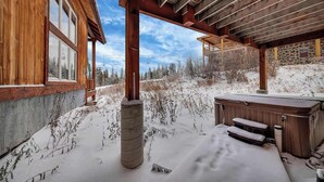 Eine Holzhütte mit überdachter Terrasse, Whirlpool und Blick auf eine verschneite Landschaft.