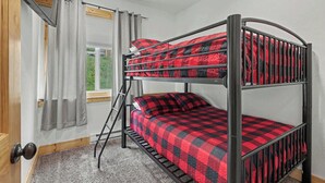 Ein Etagenbett mit karierter Decke, ein Fenster mit Vorhängen und eine Tür mit Klinke.
