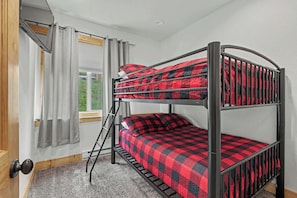 A bunk bed with a checkered blanket, a window with curtains, and a door with a knob. - Kussy Slopeside Chalet at Terry Peak (Lead)