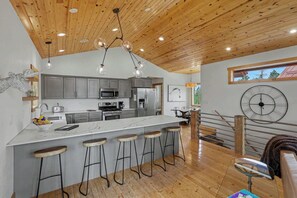 A modern kitchen with a central island, bar stools, stainless steel appliances, and a wooden ceiling. - Kussy Slopeside Chalet at Terry Peak (Lead)