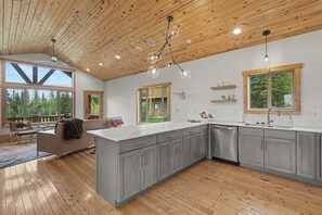 A spacious kitchen with a large island, wooden ceiling, and large windows offering views of the outdoors. - Kussy Slopeside Chalet at Terry Peak (Lead)