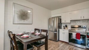 Une cuisine moderne avec des meubles blancs, des appareils en acier inoxydable et un coin repas comprenant une table et des chaises en bois.