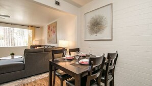 Un coin repas avec une table dressée pour quatre personnes, un canapé, une lampe et une œuvre d’art encadrée accrochée au mur.