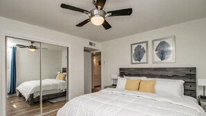 Une chambre à coucher avec un grand lit, un ventilateur de plafond, un miroir et deux œuvres d’art accrochées au mur.