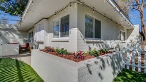 Une maison de plain-pied avec un porche abrité, un petit jardin fleuri et une clôture blanche.