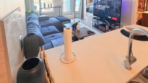 A modern living room with a sofa, TV, and kitchen area. - Condo Downtown (Beltline) w/ Underground Parking (Calgary)