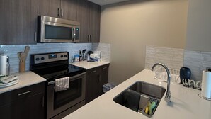 A modern kitchen with dark cabinets, stainless steel appliances, a white countertop, and a ceiling light fixture. - Condo Downtown (Beltline) w/ Underground Parking (Calgary)