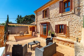 A stone building with a patio area featuring wicker furniture, a table, and potted plants. - VILLA SA COSTA CALVIÀ (Calvià)