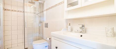 A bathroom with a shower, toilet, sink, and cabinets.