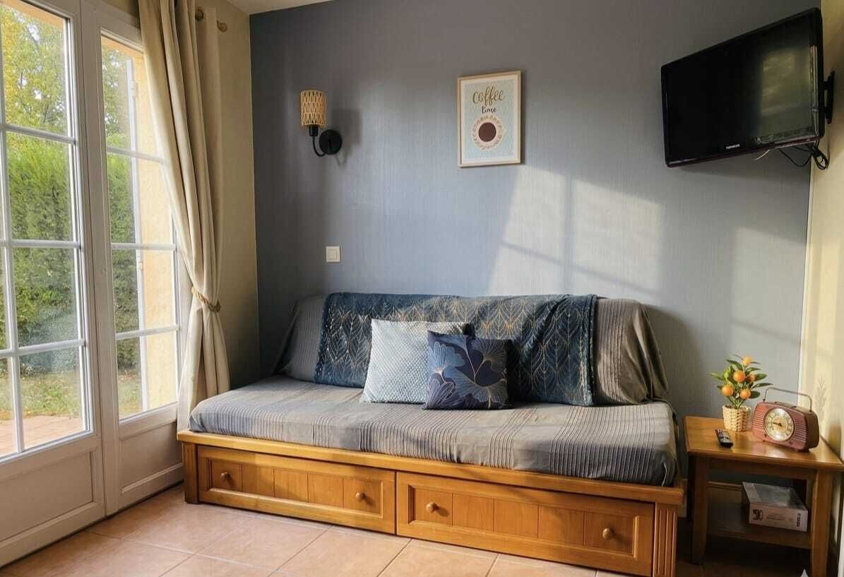 Ein Zimmer mit einer Couch, einem Fernseher, einer Wandleuchte und einem Fenster mit Vorhängen.