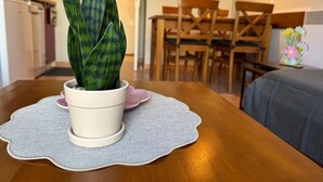 Uma planta em vaso sobre uma mesa com um jogo americano, uma mesa de jantar, cadeiras e um relógio na parede.