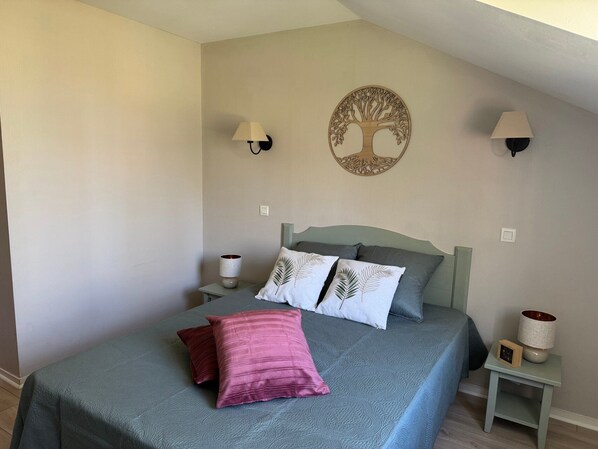 A bedroom with a bed, two wall-mounted lamps, a wall art piece, and a bedside table with a lamp and a clock.
