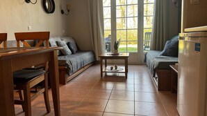 Um espaço compacto para viver com um sofá, uma mesa de jantar, uma pequena mesa com uma planta e uma geladeira.