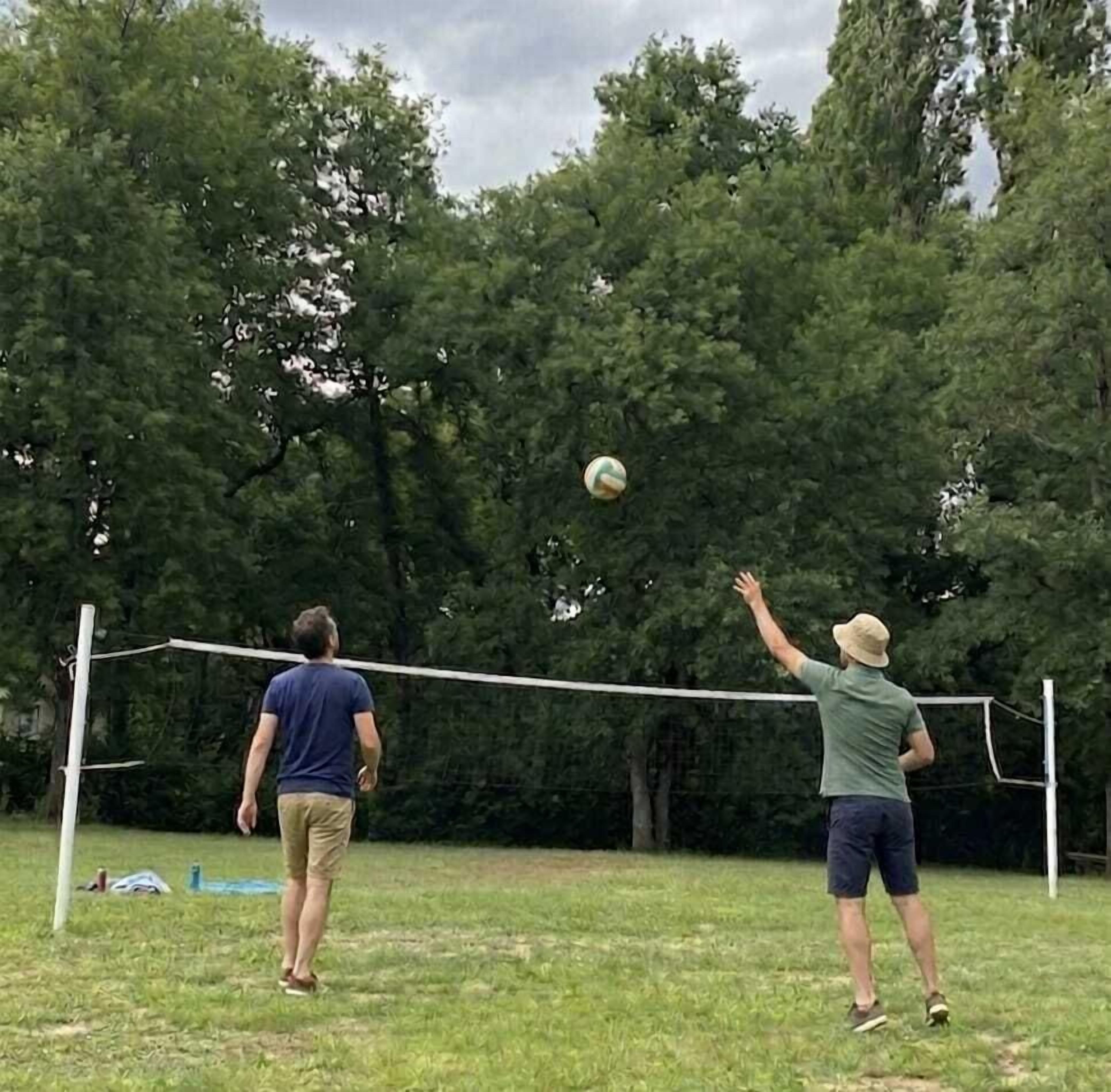 Two people playing volleyball in an outdoor setting with a net and trees in the background.