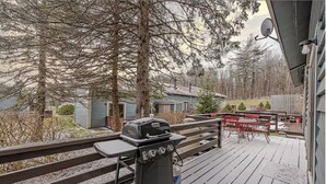 A deck with a grill, outdoor furniture, and a view of houses and trees.