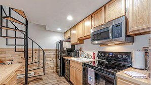 A kitchen with wooden cabinets, a stainless steel microwave, a stove, and a wooden staircase.