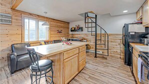 A kitchen with a central island, wooden walls, a spiral staircase, and a bar area with stools.