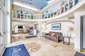 Eine geräumige Lobby mit hoher Decke, einer zentralen Sitzecke und einem Wandbild mit tropischer Landschaft.