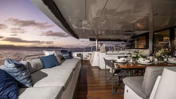 A yacht deck with a sofa, dining table, and bar area.