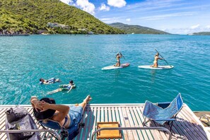 A boat deck with paddleboarders, a lounge chair, and a small table. - Floating Villa: All-Inclusive Yacht Vacation with Captain & Chef - 8 Guests (Tortola)