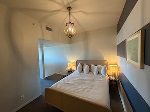 A hotel room with a bed, two bedside tables with lamps, a chandelier, a framed quote on the wall, and a door leading to another room. - Sleek 2 Bedroom Apt. Downtown Austin! (Austin)