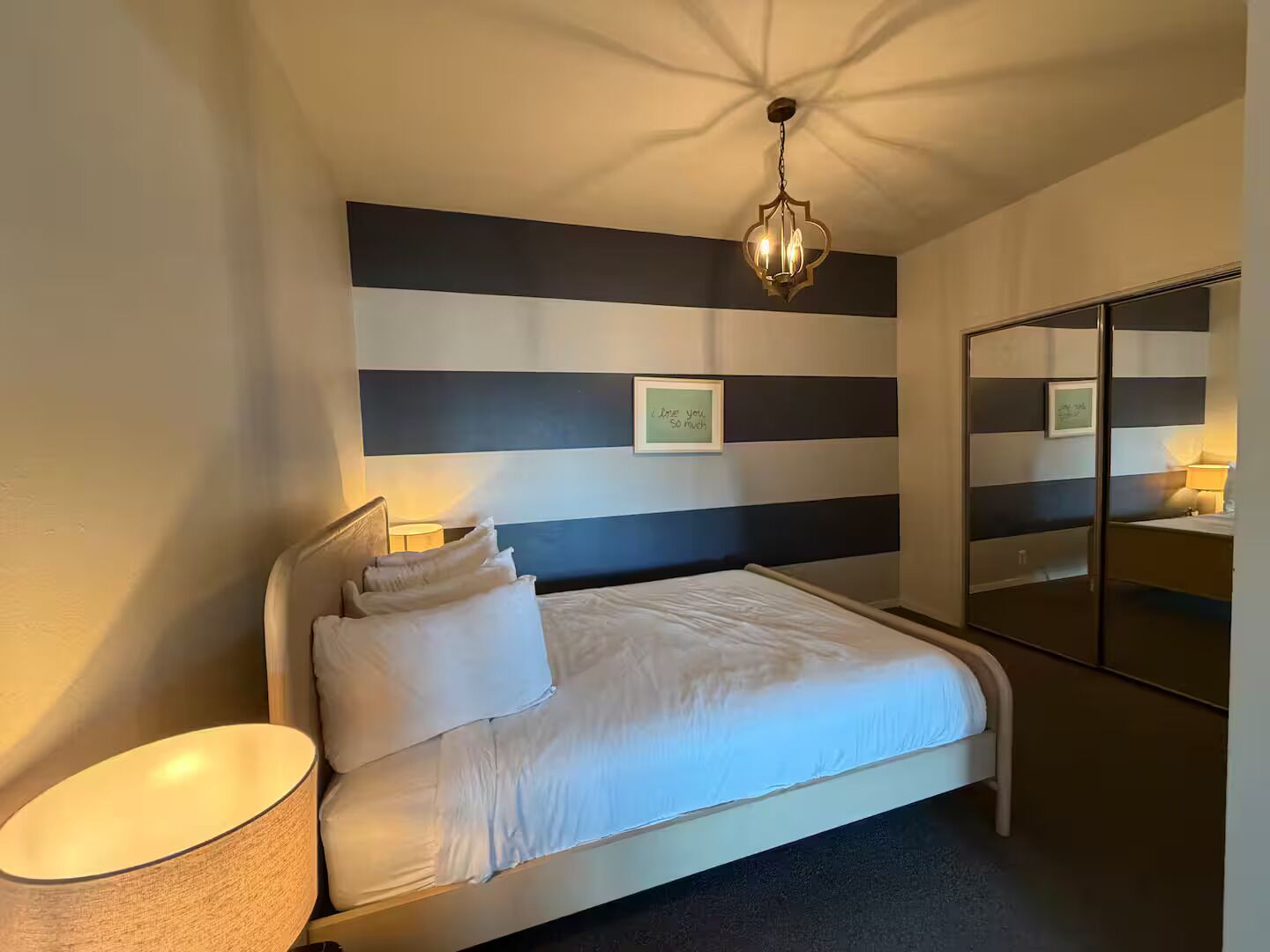 A modern bedroom with a bed, bedside lamps, a large mirror, and a ceiling light fixture.