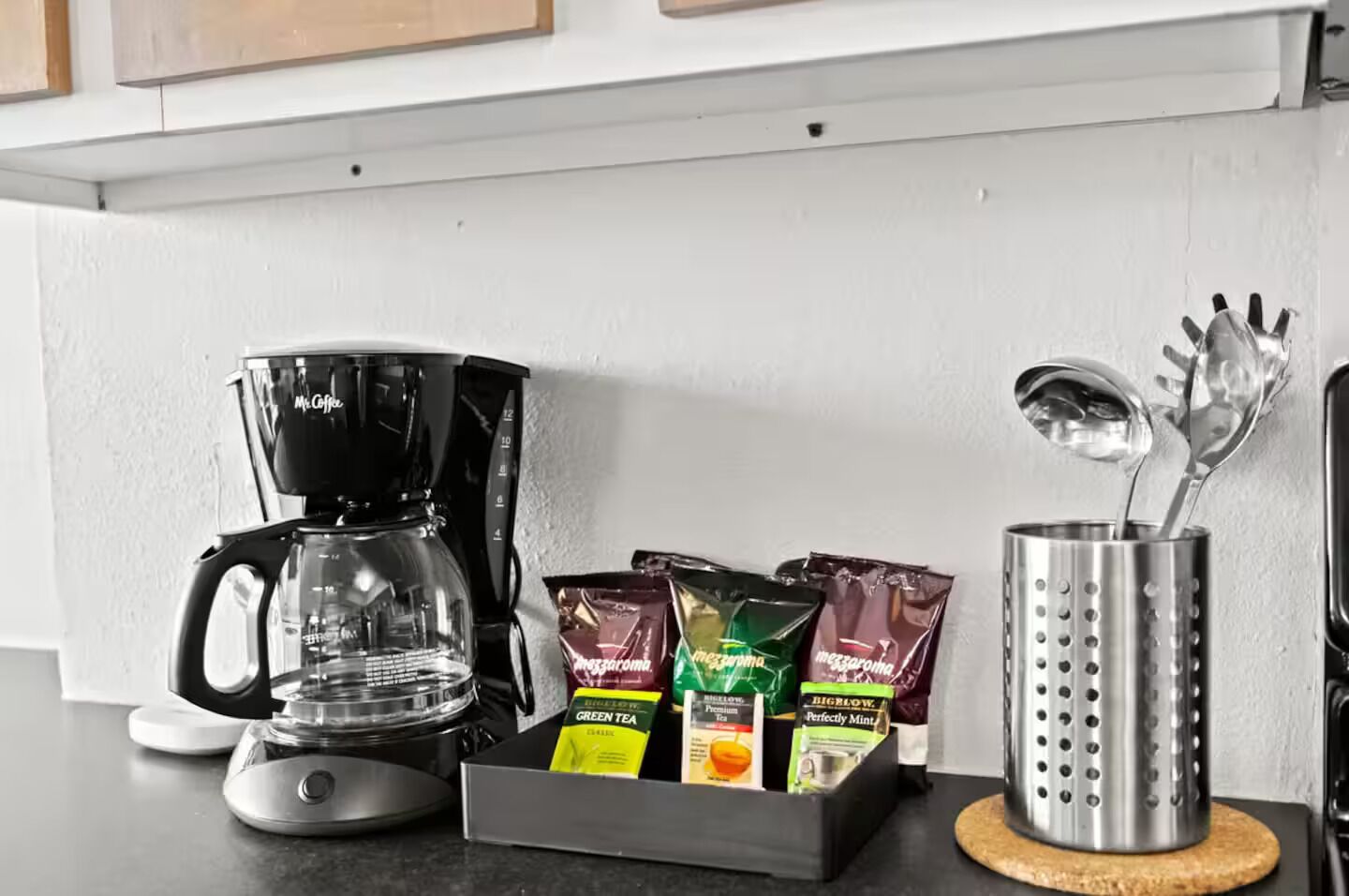 Un comptoir de cuisine avec une machine à café, des sachets de thé et un porte-ustensiles.