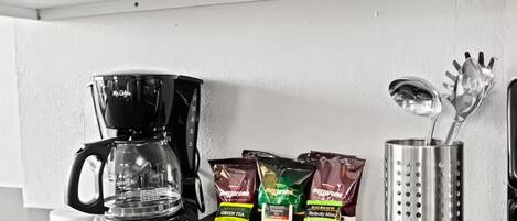 Un comptoir de cuisine avec une machine à café, des sachets de thé et un porte-ustensiles.