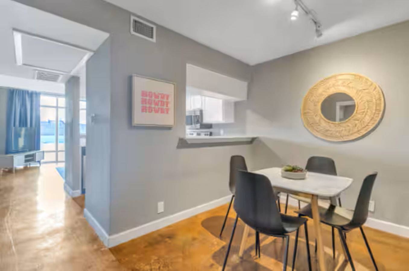 A modern dining area with a white table, black chairs, and a decorative mirror on the wall.