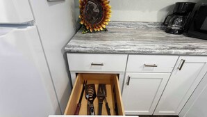 Una cocina con encimera de mármol, cafetera y un cajón con utensilios de cocina.