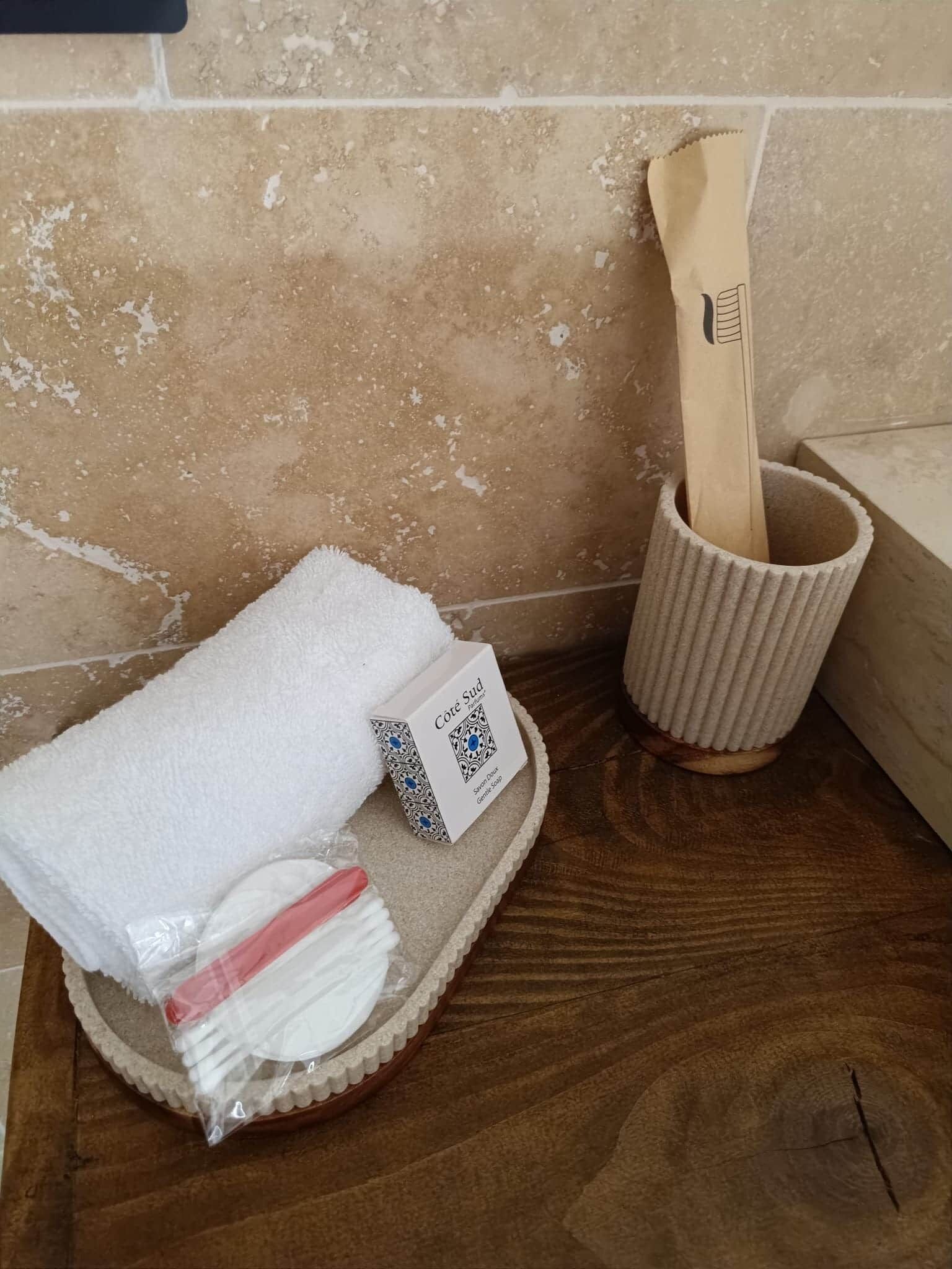 A bathroom with a wooden bath mat, a white towel, a toothbrush, and a wooden brush in a cup.