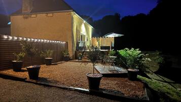 Un espace extérieur bien éclairé, aménagé en patio, avec un chemin de gravier, des plantes en pot, une clôture en bois et un bâtiment dont on aperçoit la porte et les fenêtres.