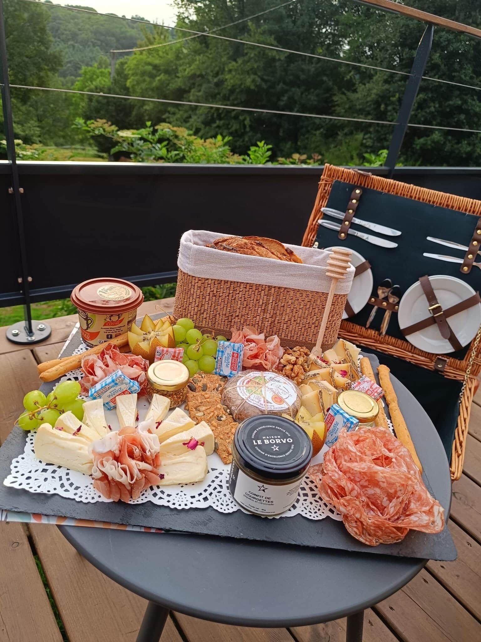 Um piquenique montado com diversos queijos, carnes e frutas sobre uma mesa ao ar livre.