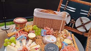 Um piquenique montado com diversos queijos, carnes e frutas sobre uma mesa ao ar livre.
