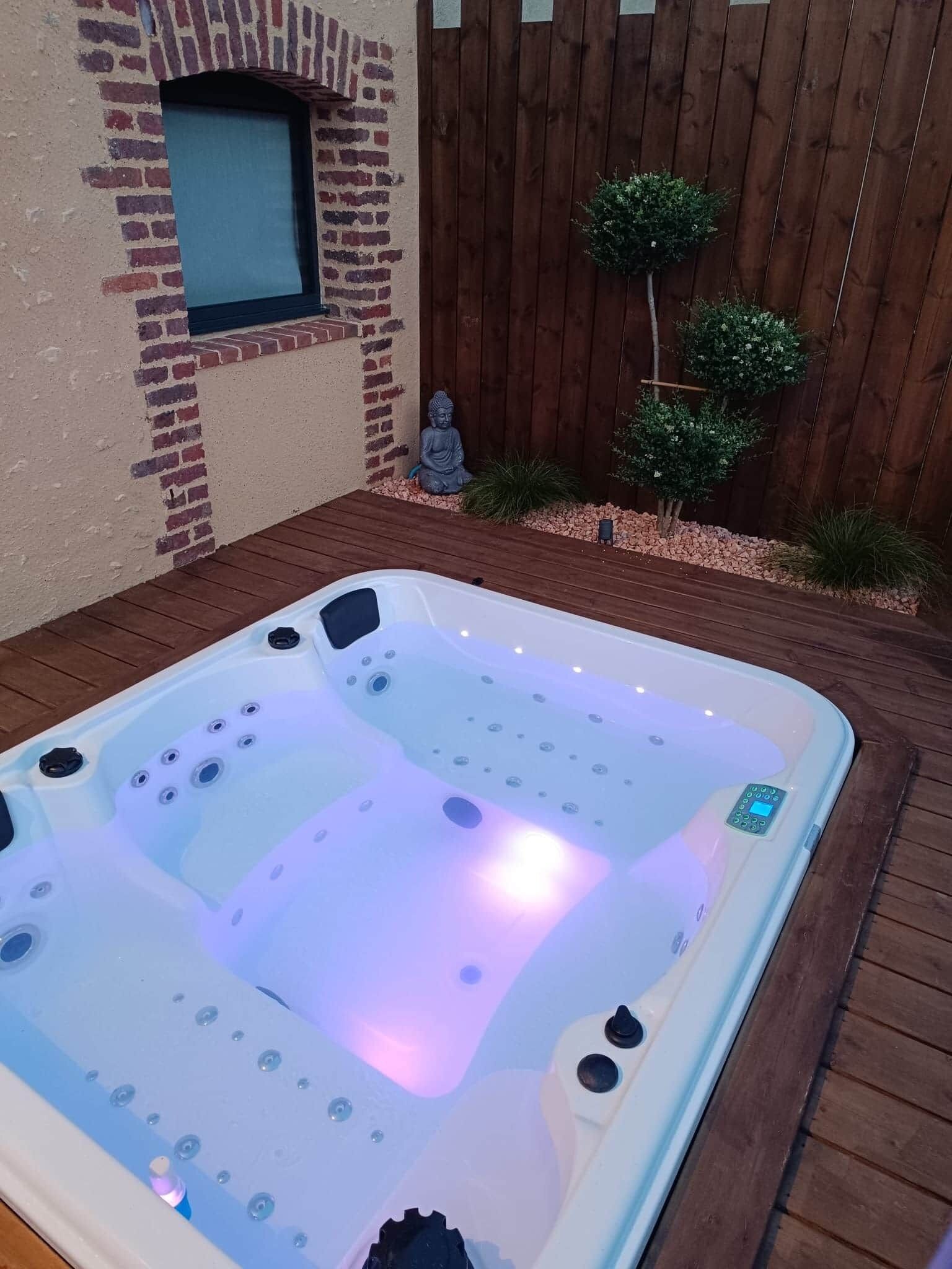 Ein Whirlpool mit Bedienfeld, umgeben von einer Holterrasse und einer Ziegelwand mit einem Fenster.