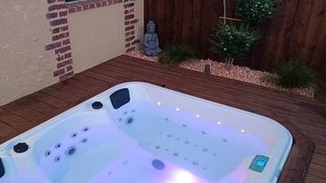 Ein Whirlpool mit Bedienfeld, umgeben von einer Holterrasse und einer Ziegelwand mit einem Fenster.