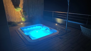 A hot tub on a wooden deck with a metal railing and a wall in the background.
