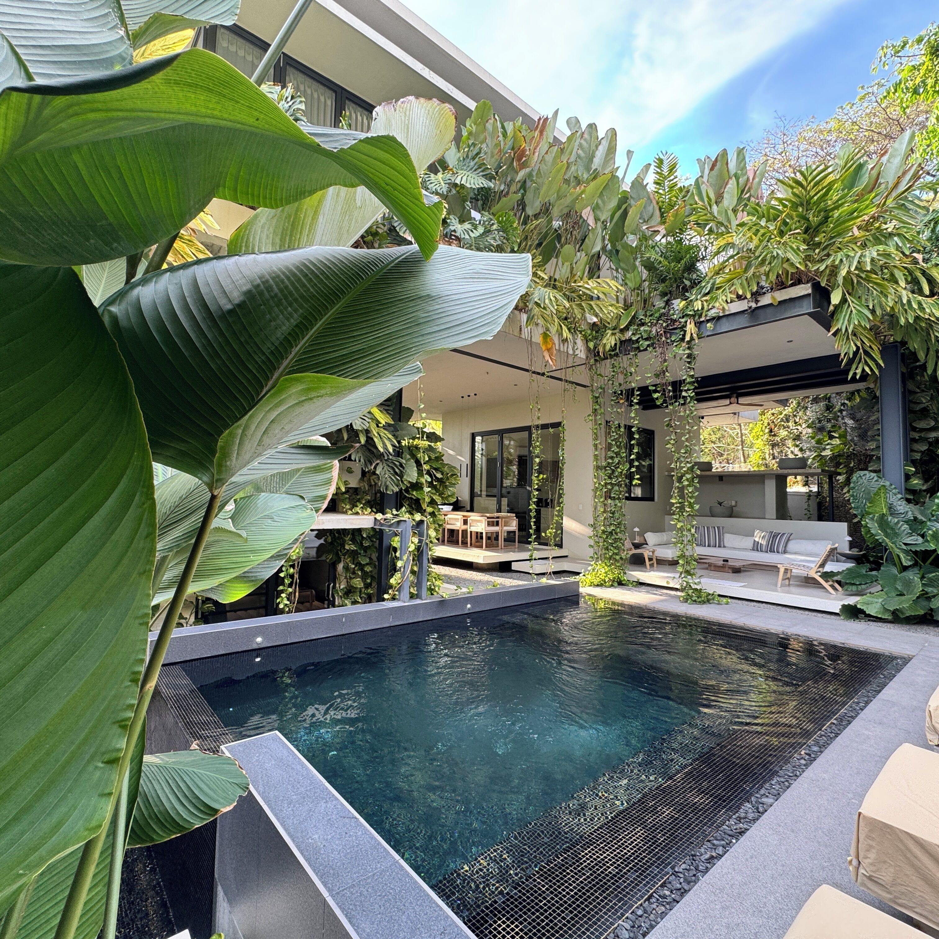 Uma área de piscina moderna ao ar livre, com espaço para sentar e vegetação exuberante.