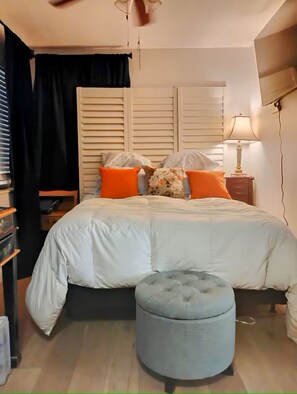 Une chambre à coucher comprenant un lit, un pouf, une table de chevet, une lampe et un téléviseur fixé au mur.