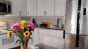 A modern kitchen with white cabinets, a stainless steel refrigerator, a microwave, and a dining table with chairs. - Private Secure BBQ Man Cave near Beach & Casinos (Hollywood)