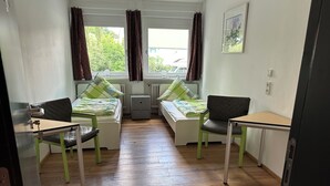 Ein Zimmer mit zwei Betten, einem Schreibtisch, einem Stuhl, einem Heizkörper und einem Fenster mit Vorhängen.