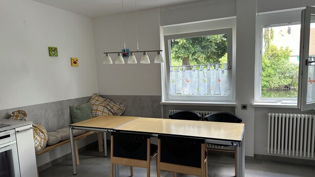 Eine moderne Küche mit Esstisch, Stühlen, einem eingebauten Ofen und einem Fenster mit Blick ins Grüne.