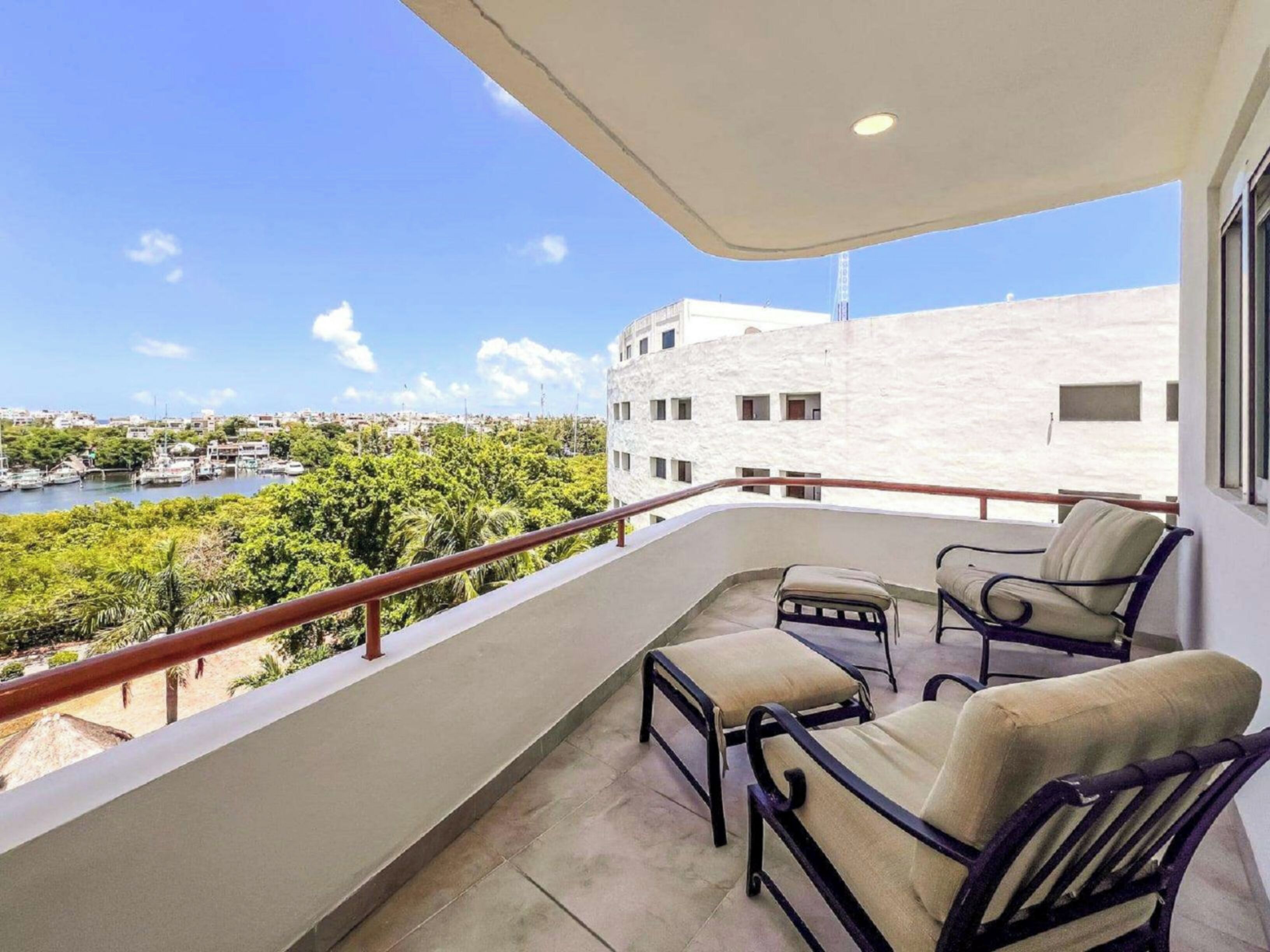 Ein Balkon mit zwei Stühlen und einem Tisch, mit Blick auf einen Yachthafen und Gebäude.