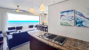 Uma cozinha moderna com bancada de granito, duas bocas elétricas e um espaço de jantar com vista para o oceano.