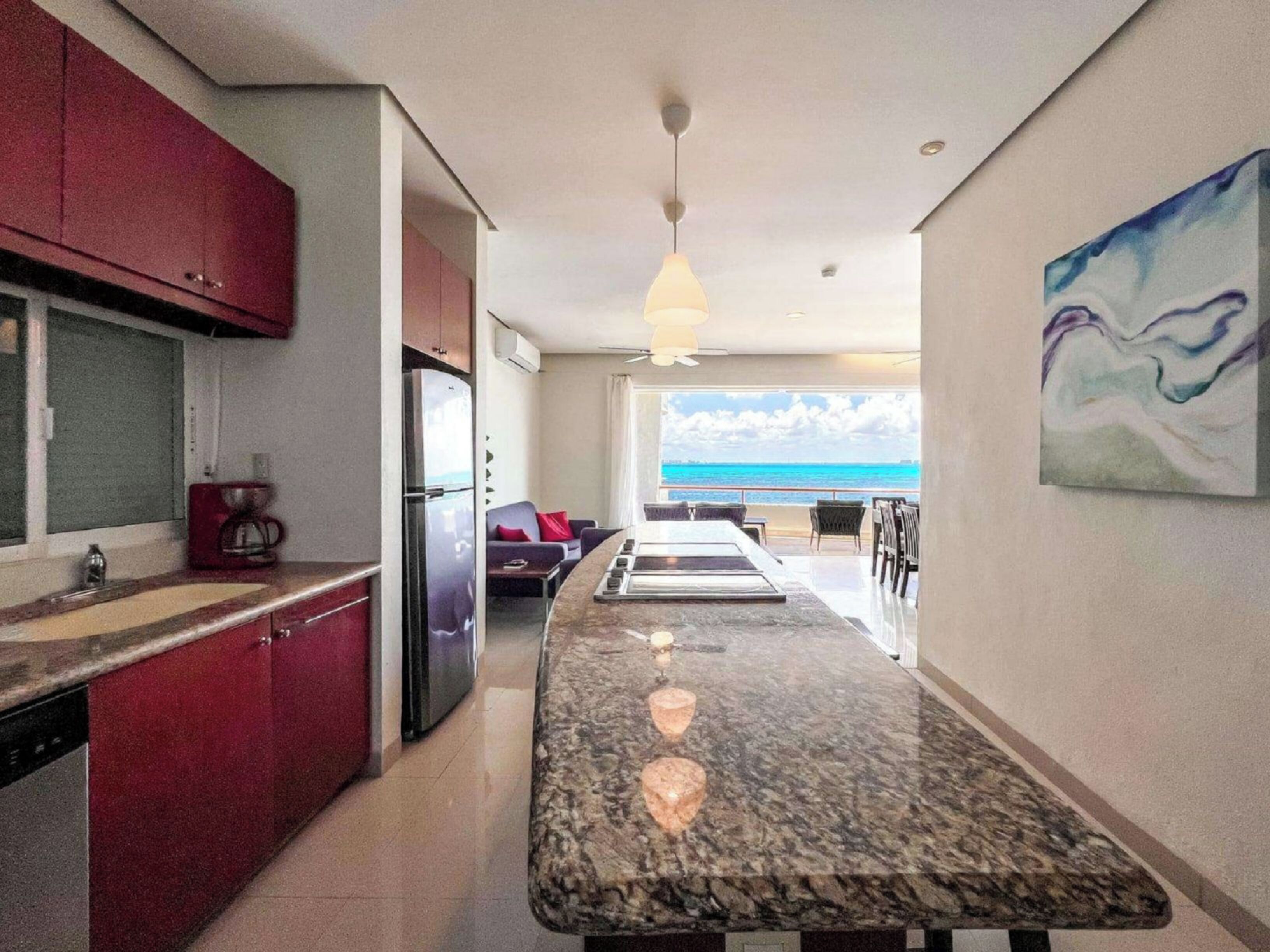 Una cucina moderna con un piano di lavoro in marmo, mobili rossi e vista sull'oceano.