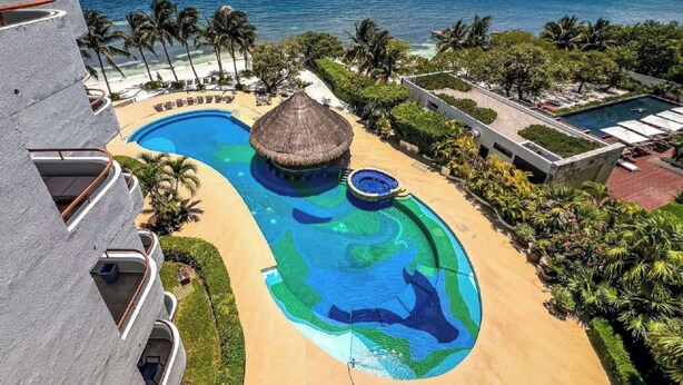 Um resort com uma grande piscina, uma estrutura com telhado de palha e vista para o oceano.