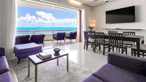 Uma sala de estar moderna com vista para o oceano, uma área de jantar e uma televisão de tela plana na parede.