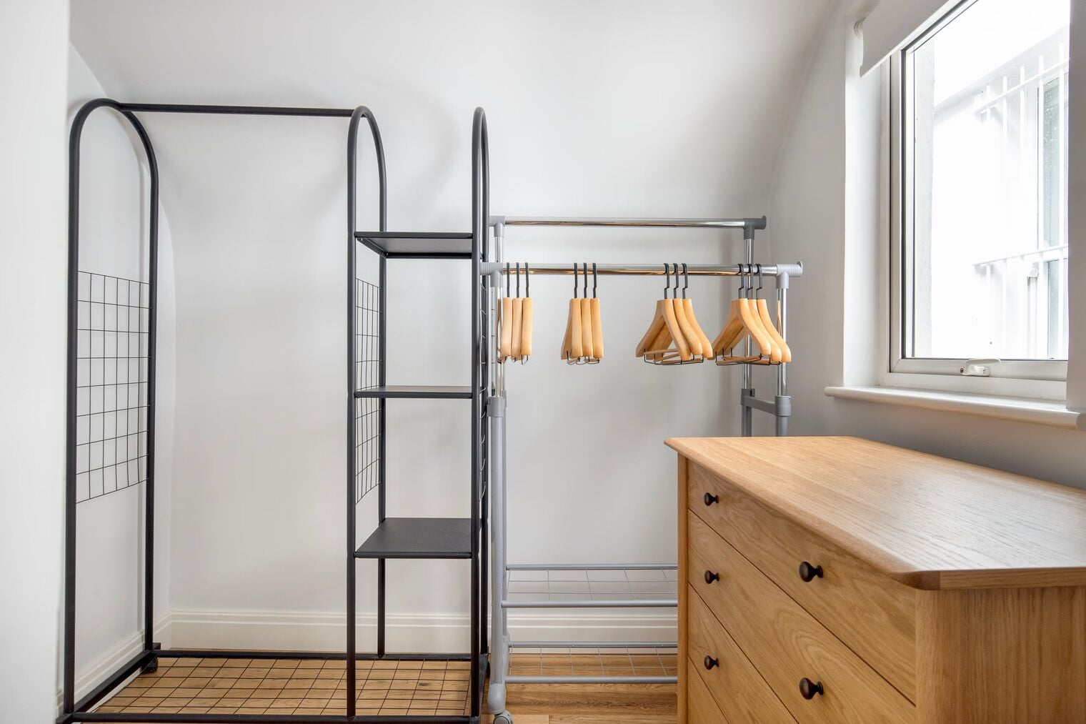 Een kamer met een metalen rek, een houten dressoir en een raam met uitzicht.